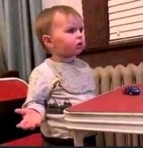 Wide-eyed toddler frozen mid-turn with one hand out in total confusion