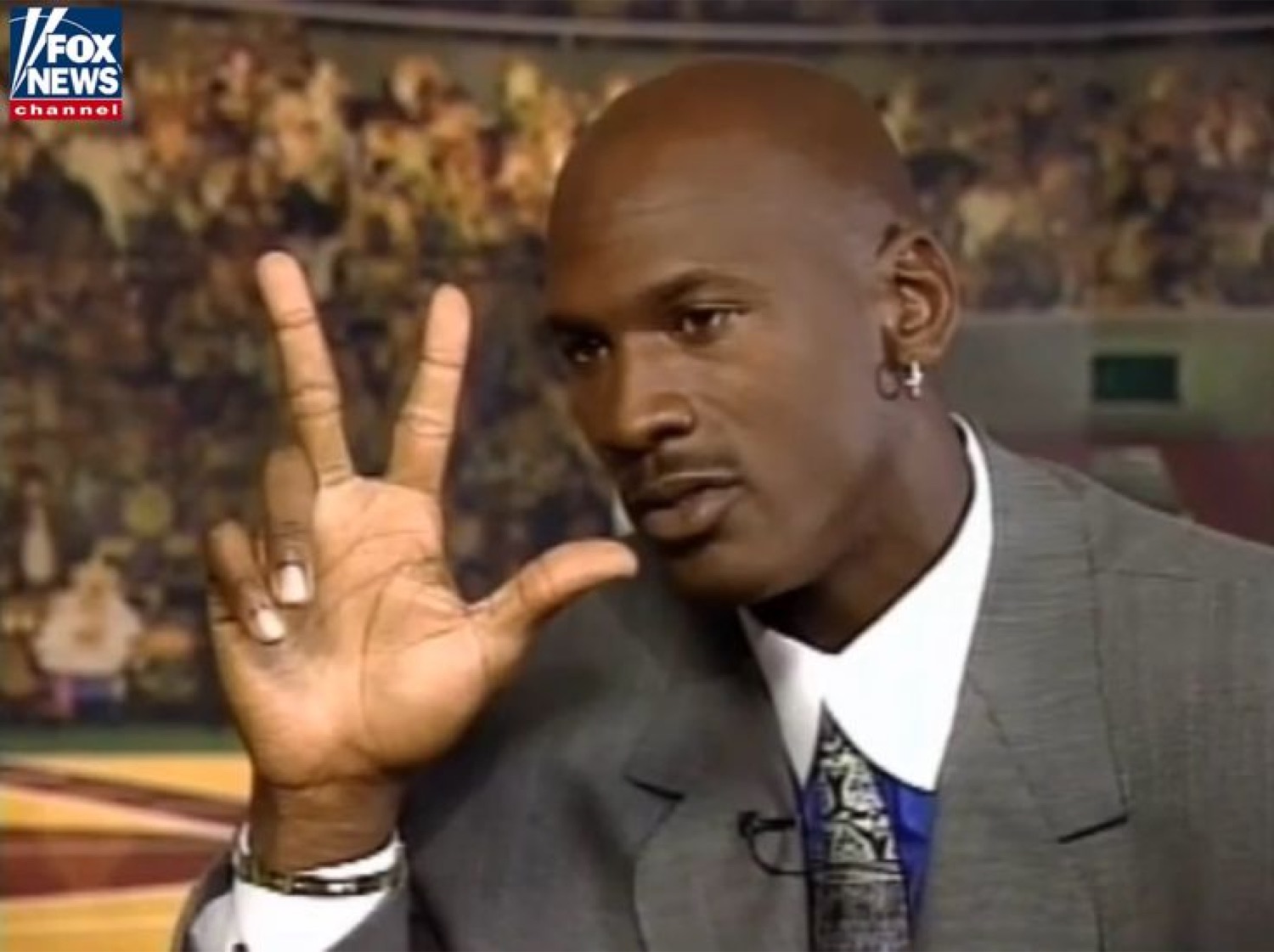 Michael Jordan in a suit holding up a hand during an interview