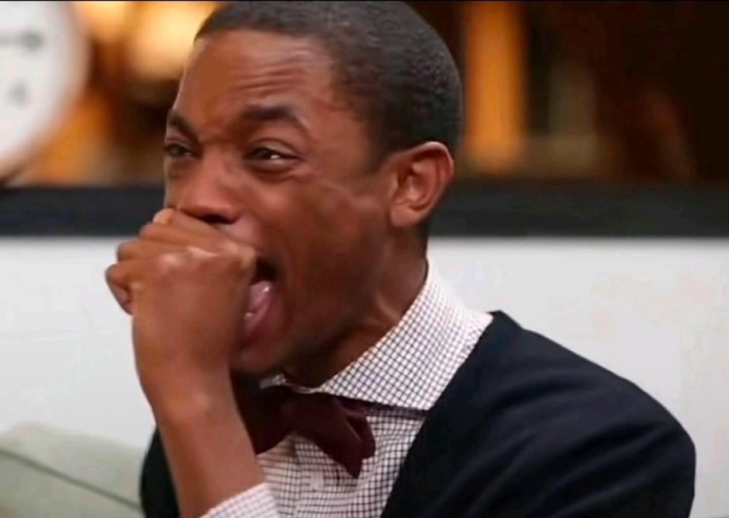 Man in a bow tie doubled over, laughing into his fist