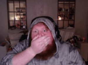 Hooded gamer with a headset covering his mouth, wide-eyed and stunned