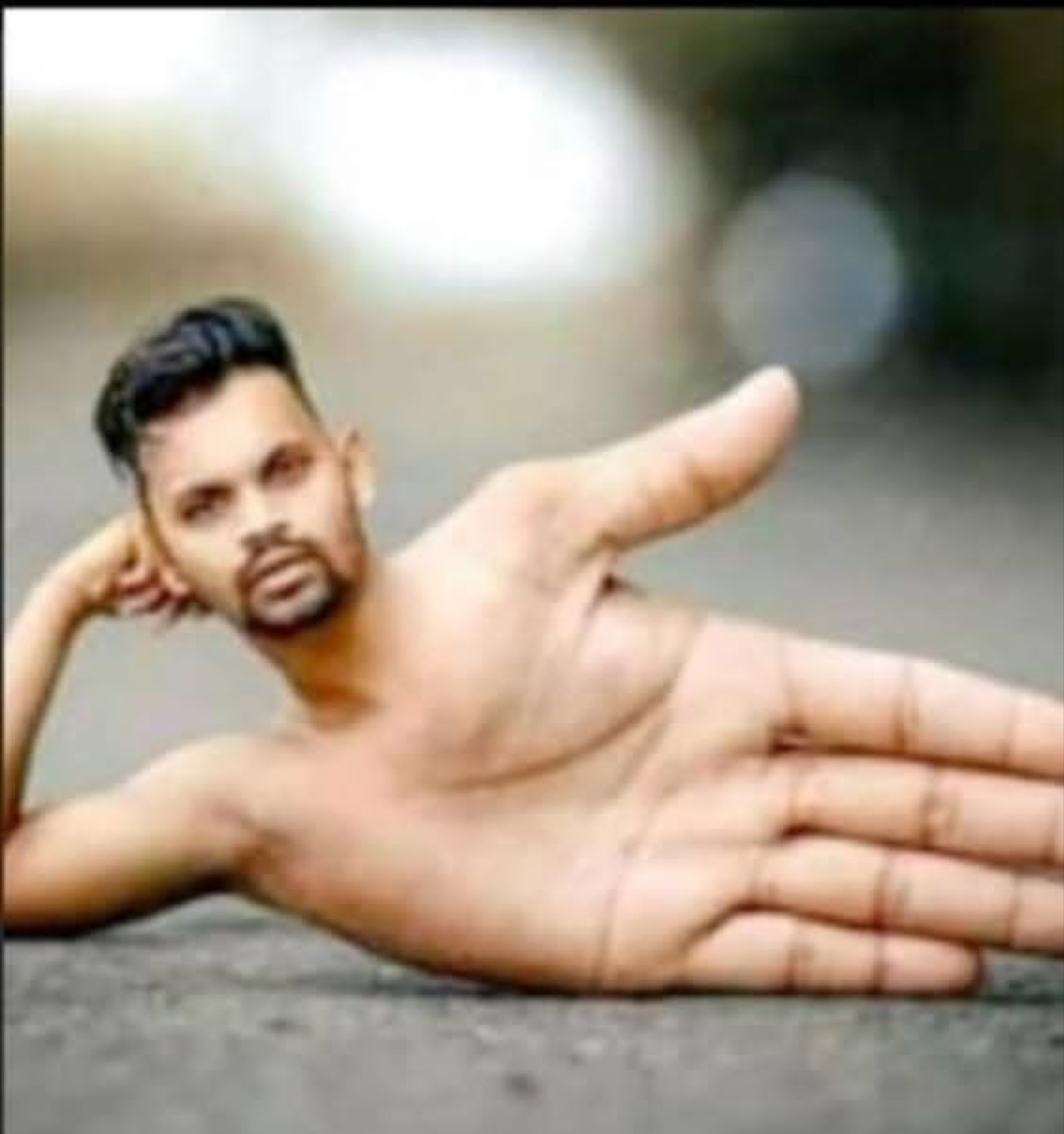 Man's head photoshopped onto a giant hand, lying on pavement in a deeply surreal pose