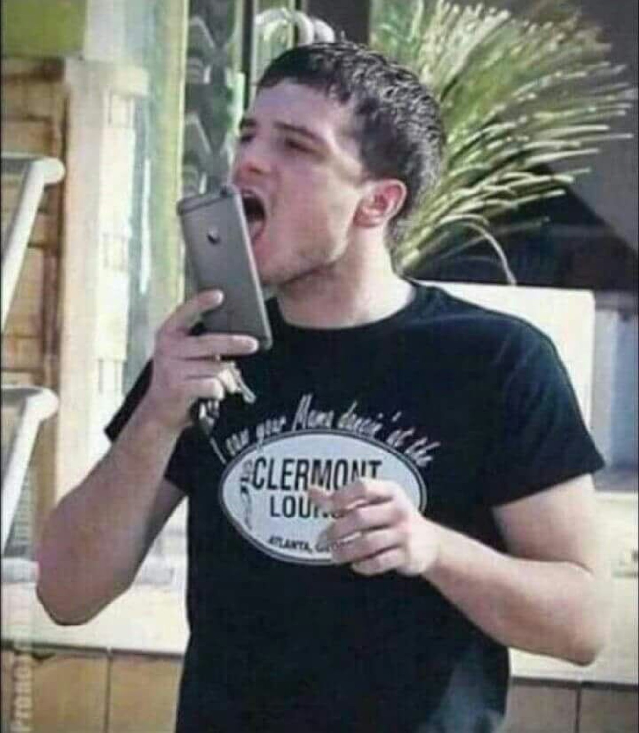 Guy in a Clermont Lounge tee cramming an entire phone into his mouth