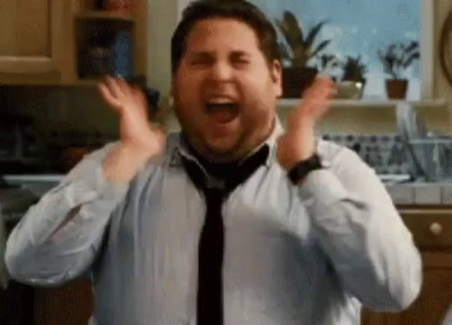 Guy in a shirt and tie screaming with both hands up in a kitchen