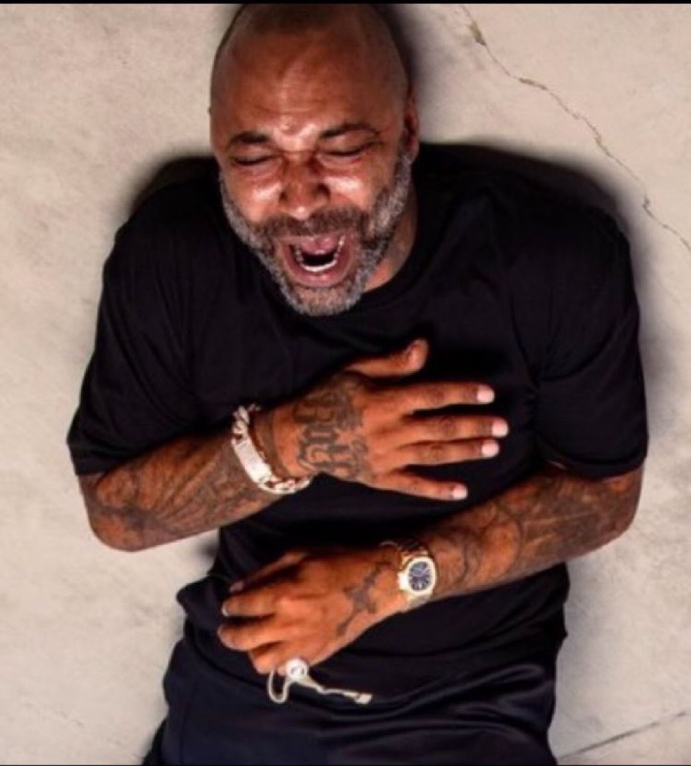 Bald tattooed man slumped against a wall clutching his chest, dying laughing