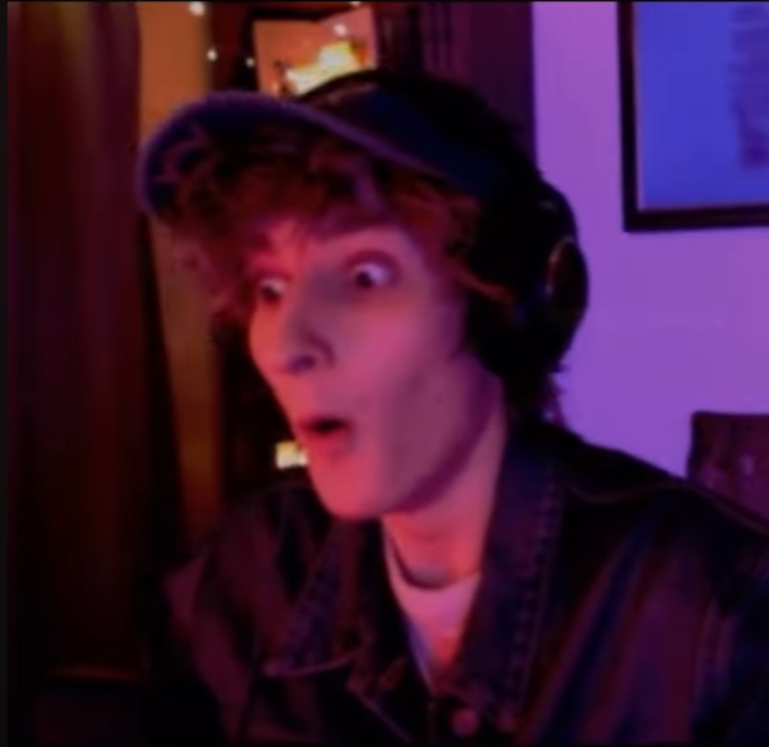 Streamer in a cap and headset with wide eyes and a dropped jaw in total disbelief under purple lighting