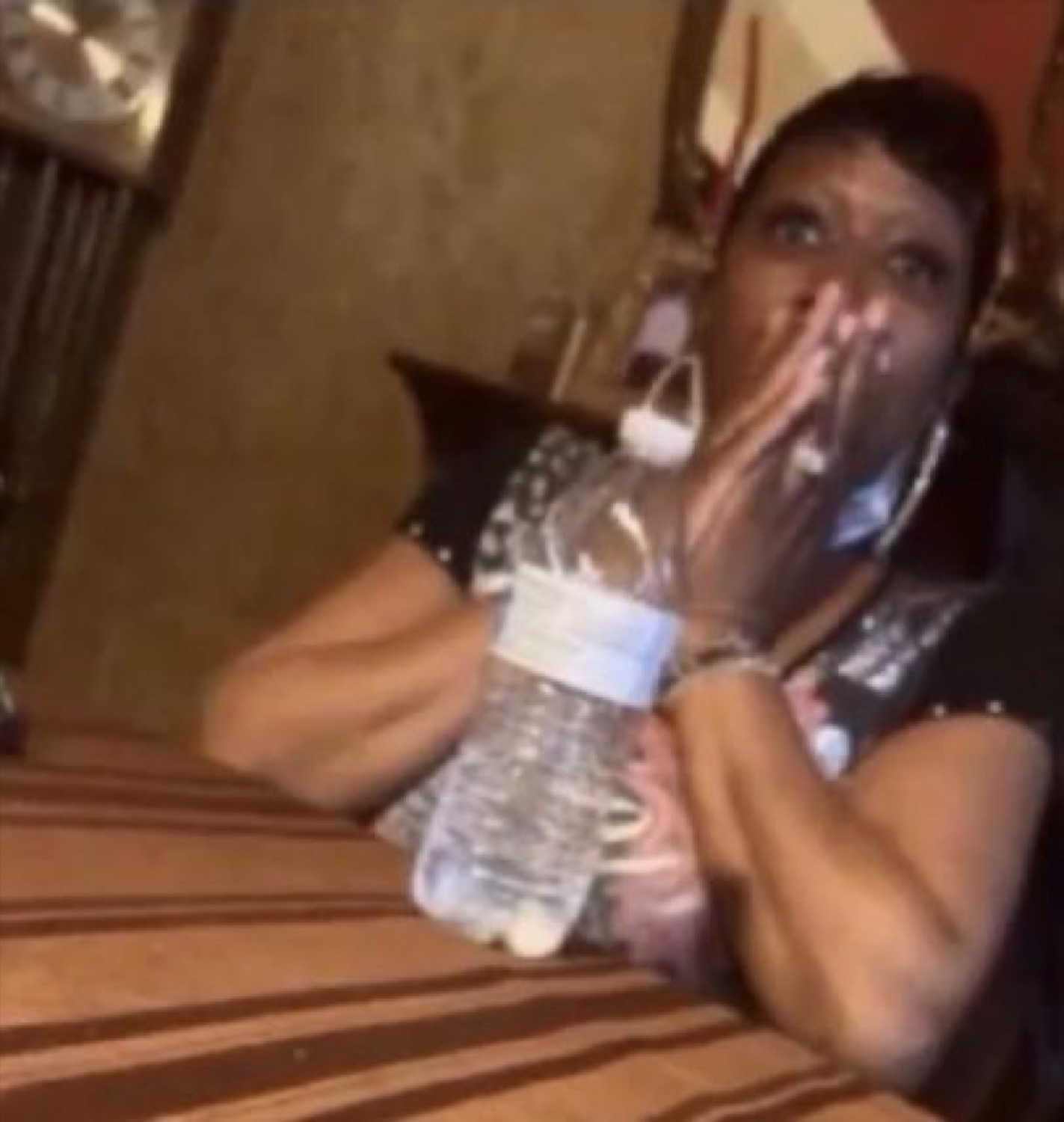 Woman clutching a water bottle with a hand over her mouth, wide-eyed in disbelief