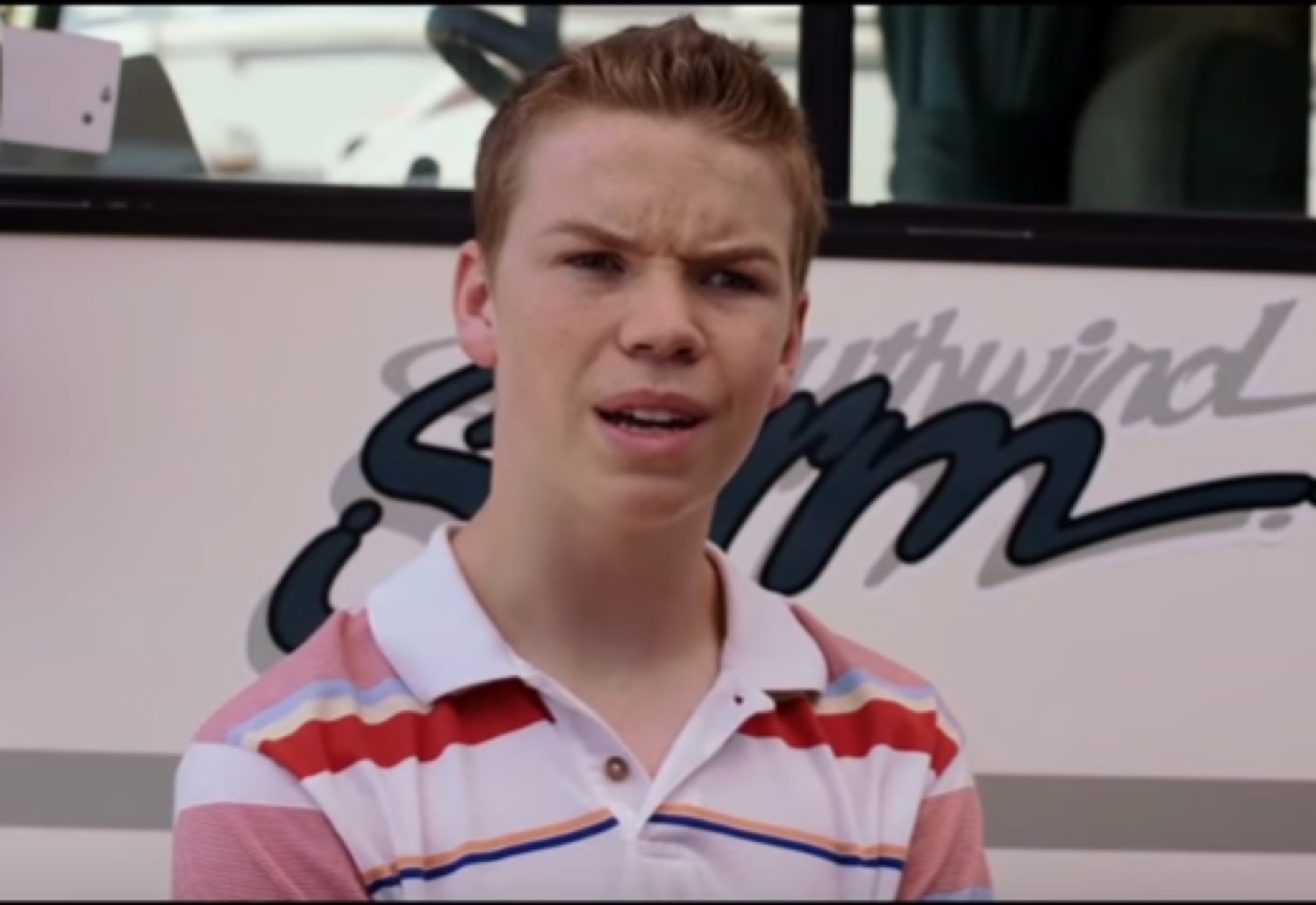 Young man in a striped polo squinting with a puzzled, judgmental frown in front of an RV
