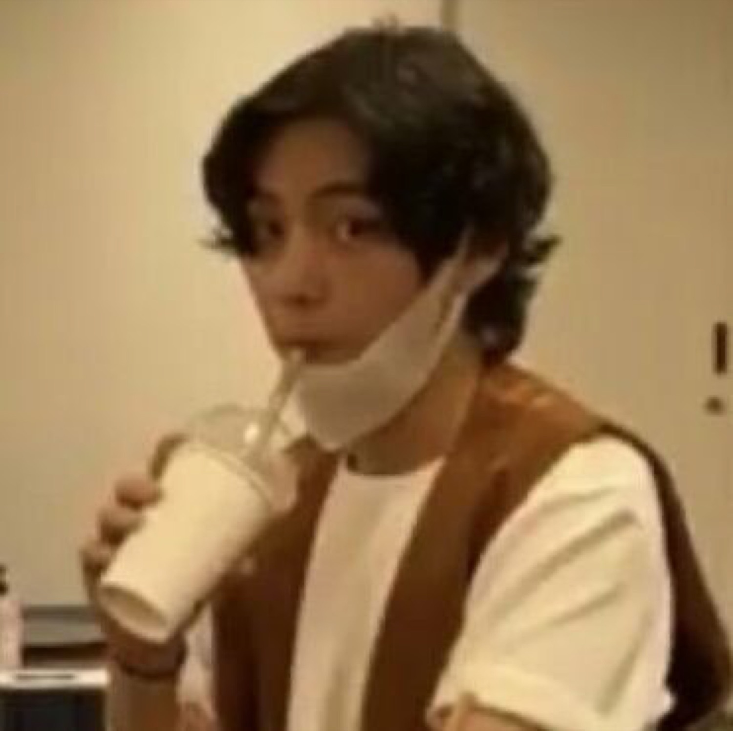 Guy with a mask around his chin sipping an iced drink through a straw, deadpan
