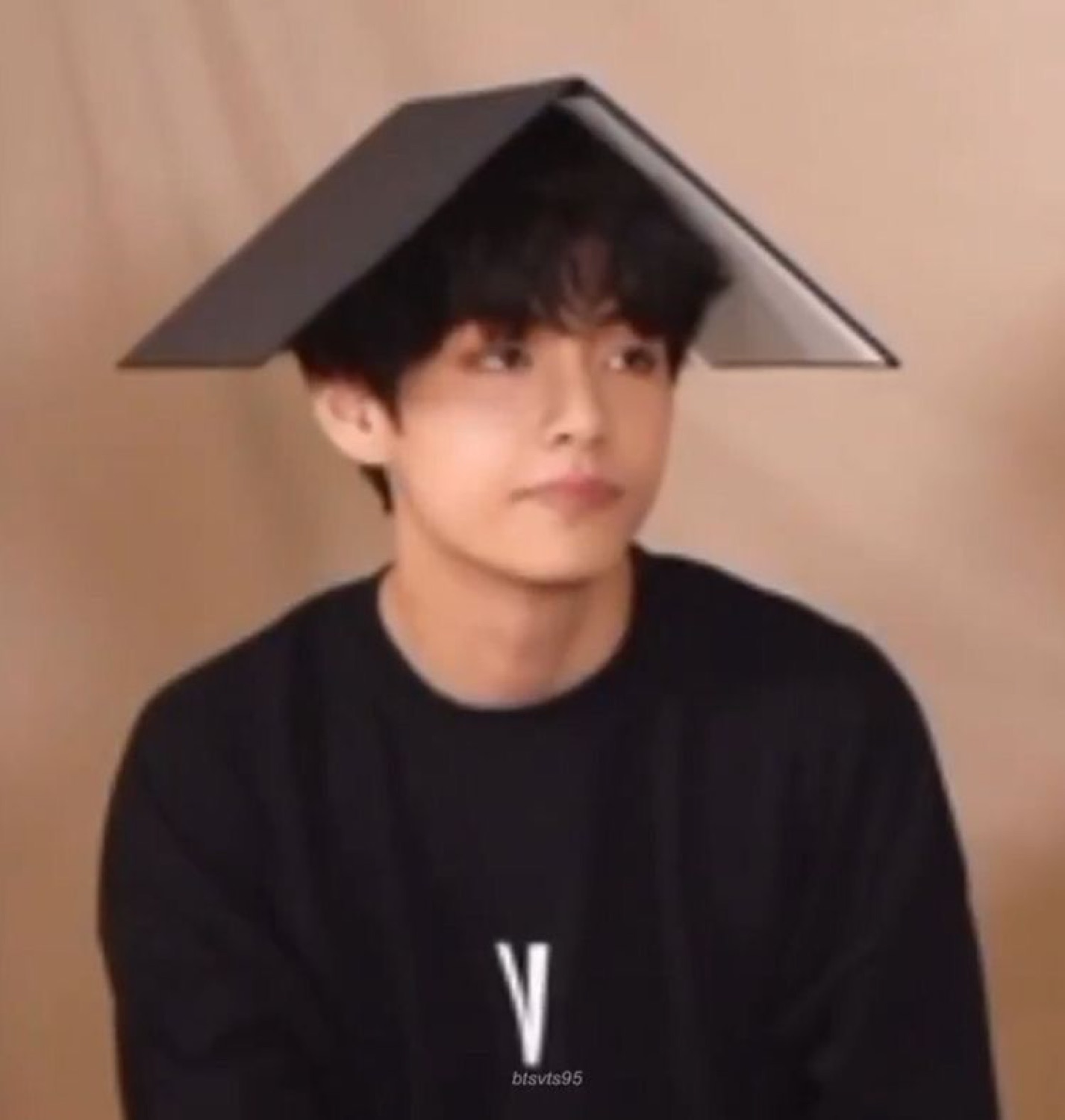 BTS's V sitting with a book balanced flat on his head, staring into space