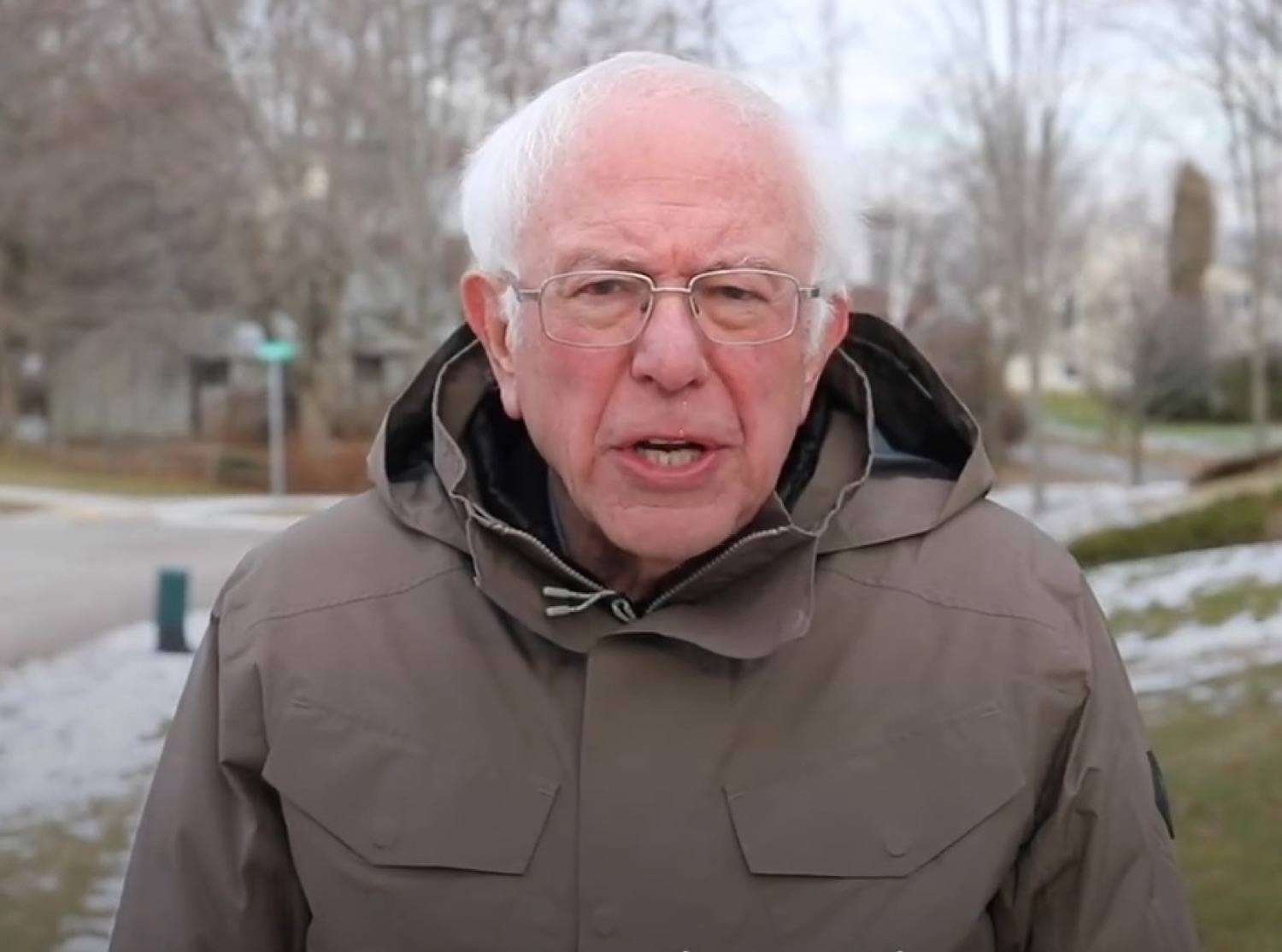 Bernie Sanders in a winter parka mid-sentence, looking a little exasperated outdoors