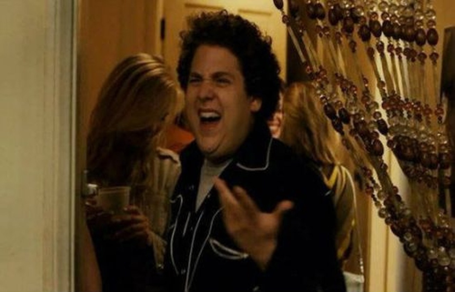 Man in a doorway laughing and gesturing wildly at a party