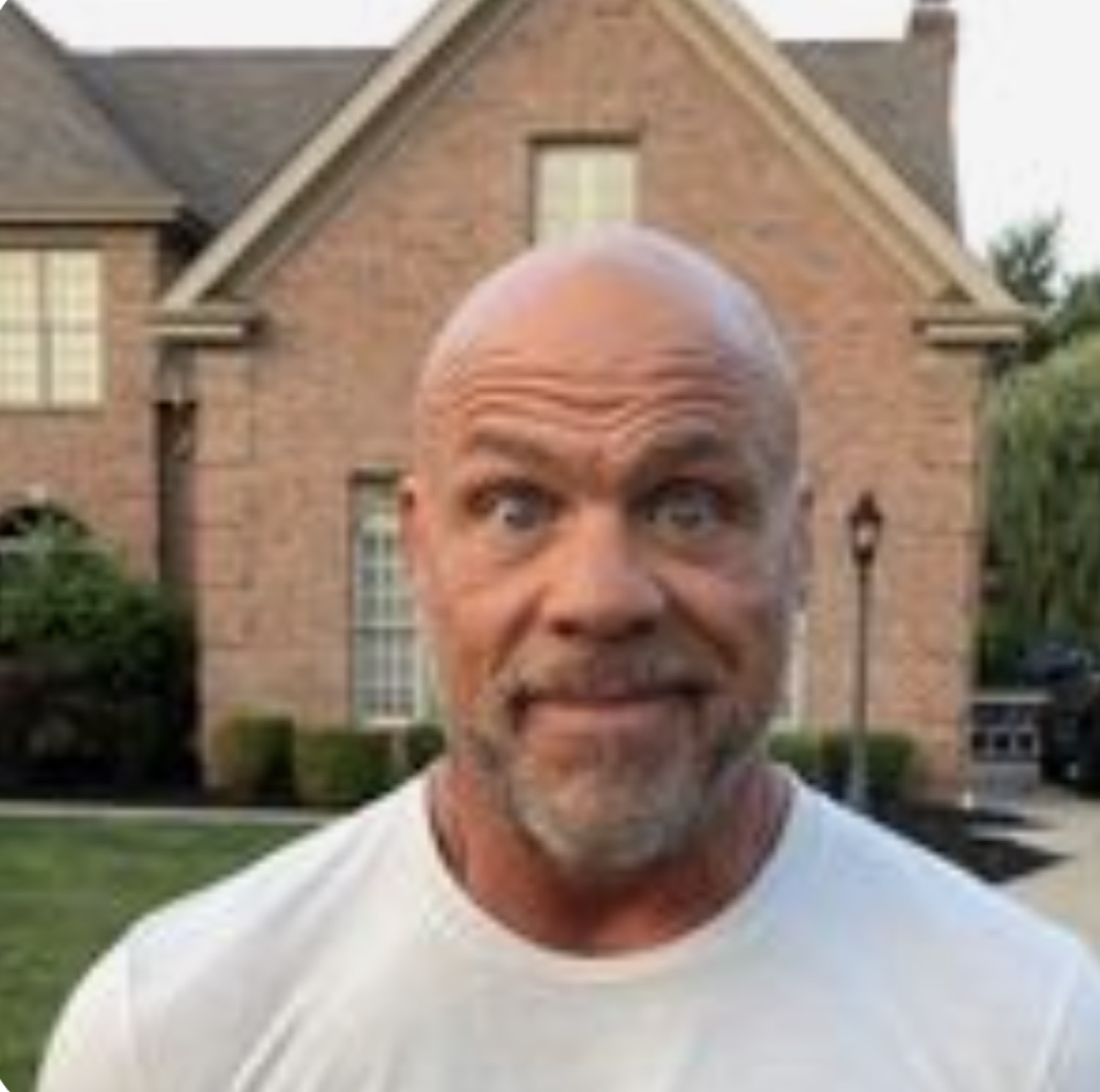 Bald bearded man outside a house making a tense, uneasy face