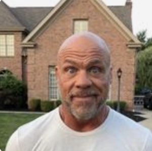 Bald bearded man outside a house making a tense, uneasy face
