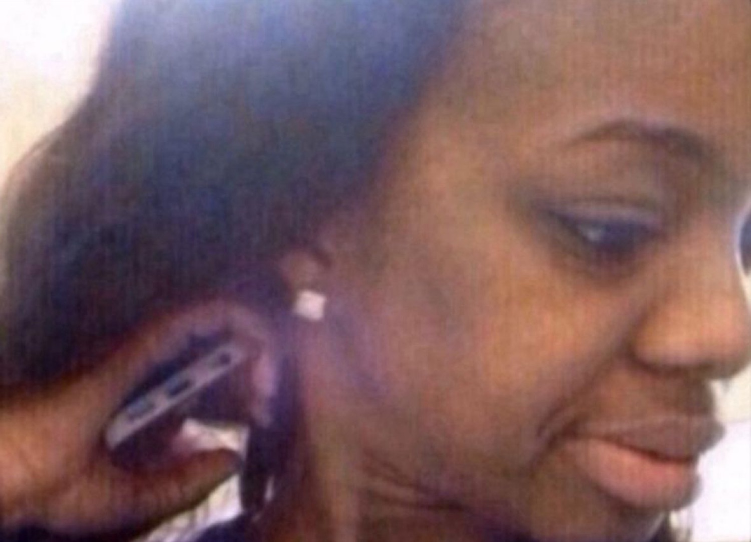 Young woman in profile giggling while someone holds a phone up to her ear