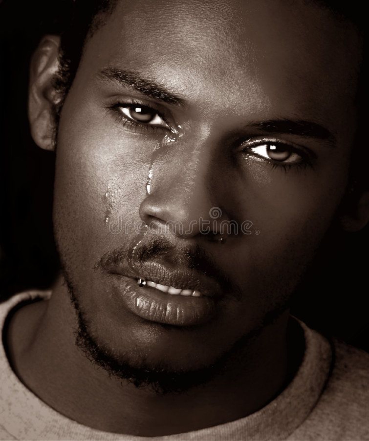 Sepia close-up of a man with a single tear running down his cheek, staring into the distance