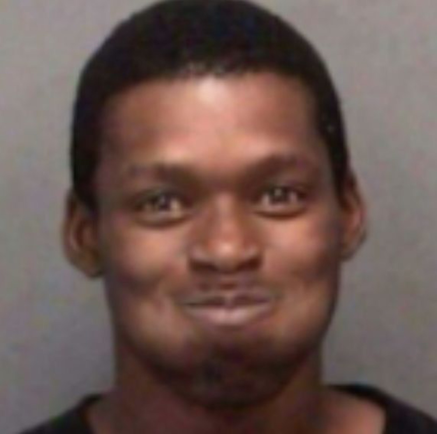 Man in a mugshot-style photo holding a faint, awkward little smirk