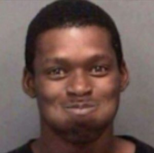 Man in a mugshot-style photo holding a faint, awkward little smirk