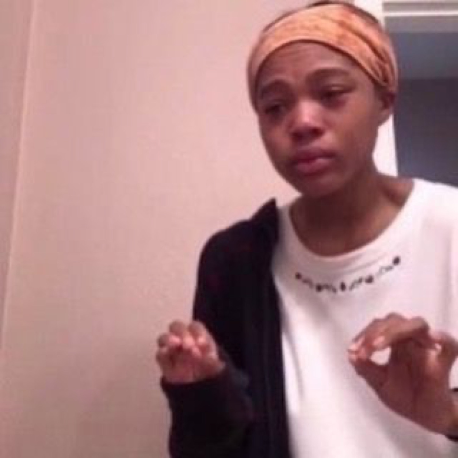 Person in a headband and hoodie crying with hands raised and shaking, visibly distressed
