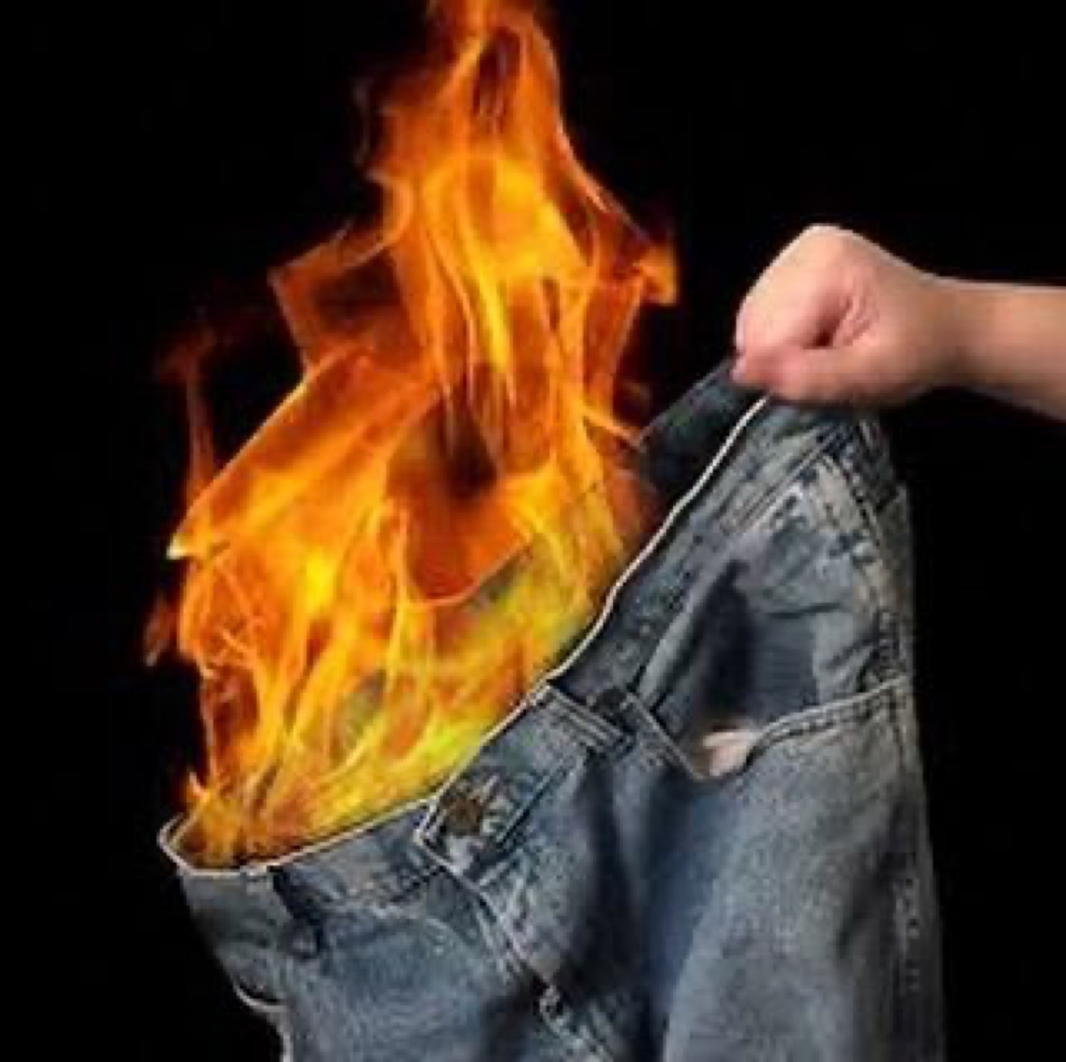 A hand holding up a pair of jeans that are literally on fire against a black background