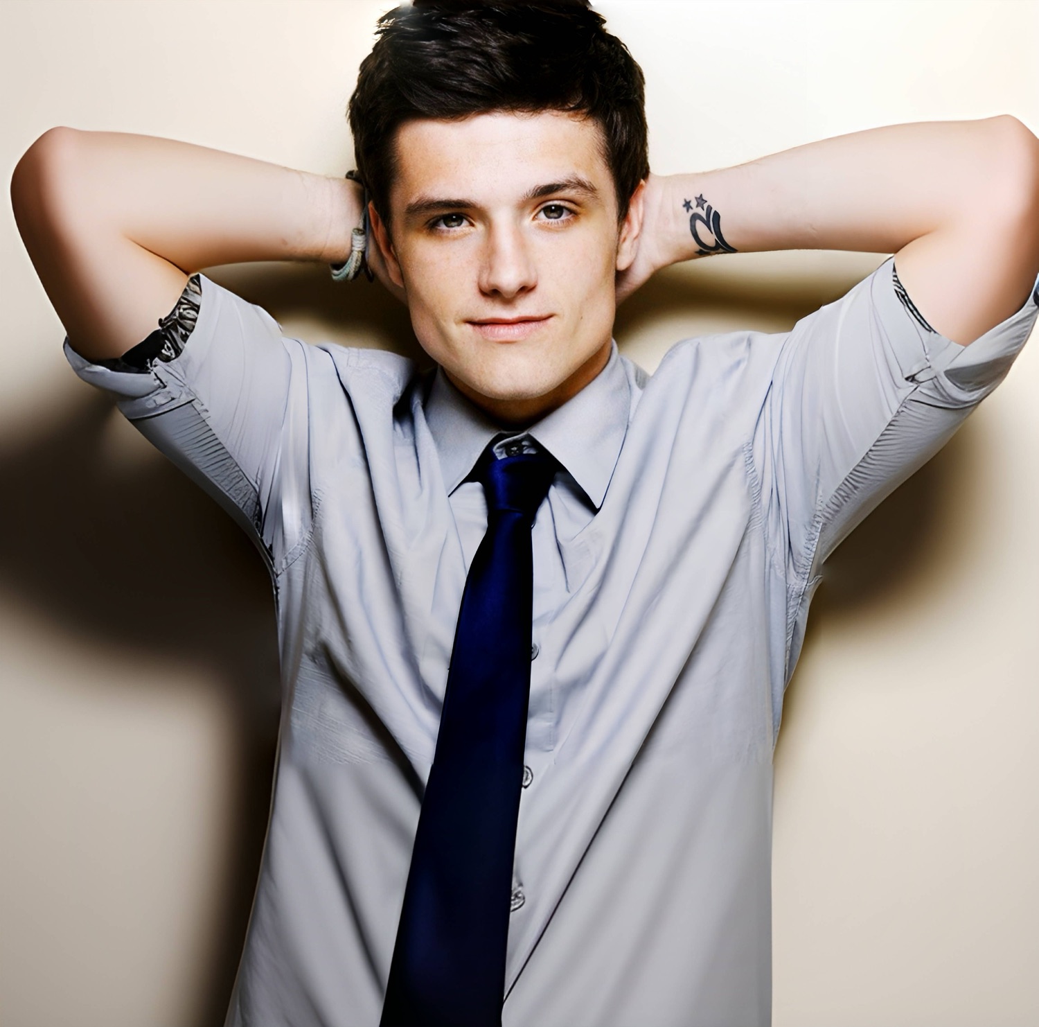 Young man in a grey shirt and dark tie leaning back with hands behind his head and a smug little smile