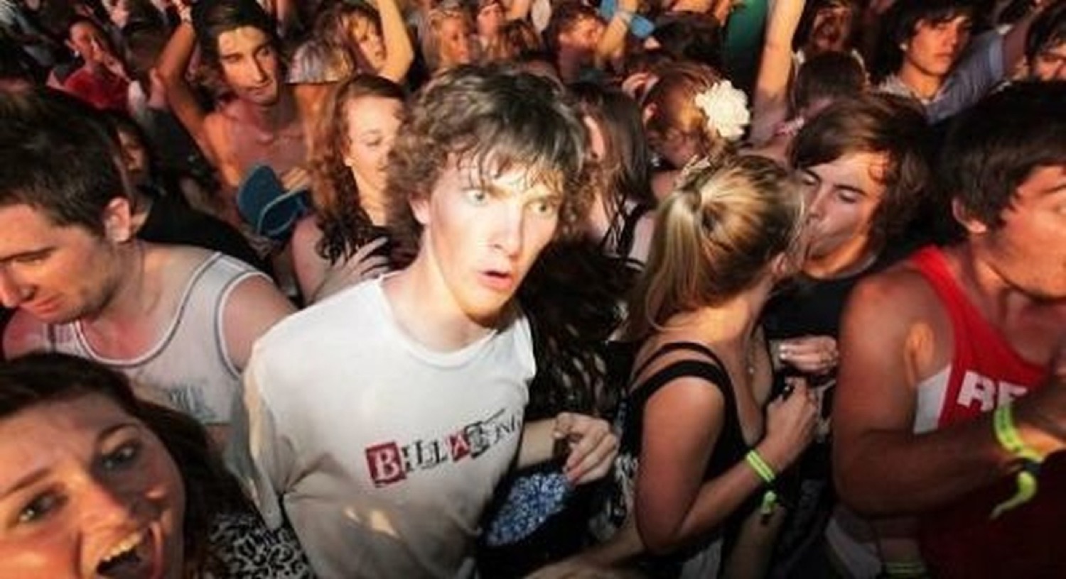 Guy in a crowded party looking lost and dazed while everyone dances around him