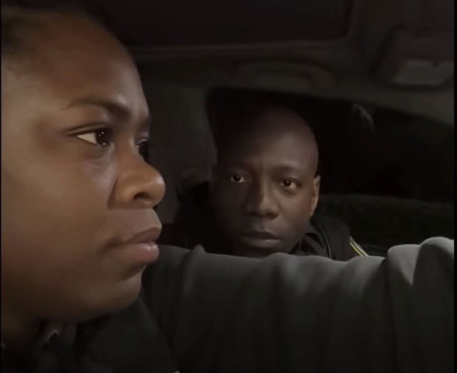A man in a car glances suspiciously at the person in front while she stares dead ahead in the dark