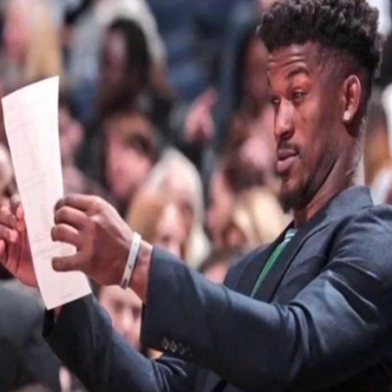 Man in a suit courtside squinting skeptically at a sheet of paper he's holding up