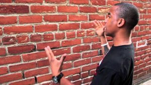 Man venting at a brick wall with his hands raised in frustration