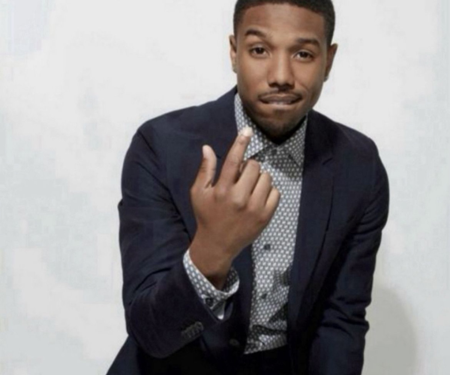Michael B. Jordan in a blazer making a come-hither gesture with a confident smirk