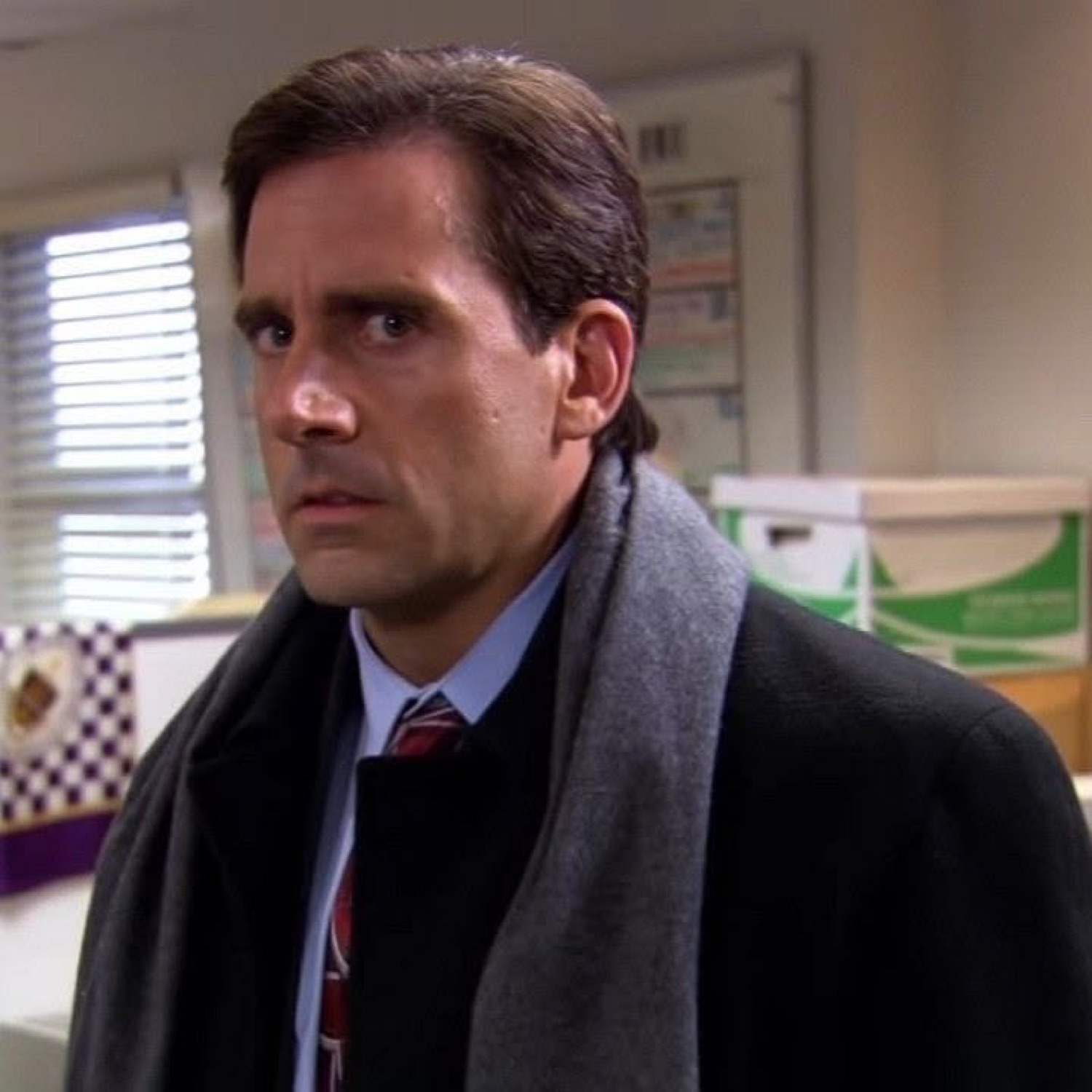 Michael Scott in a scarf and coat staring with wide worried eyes in the office