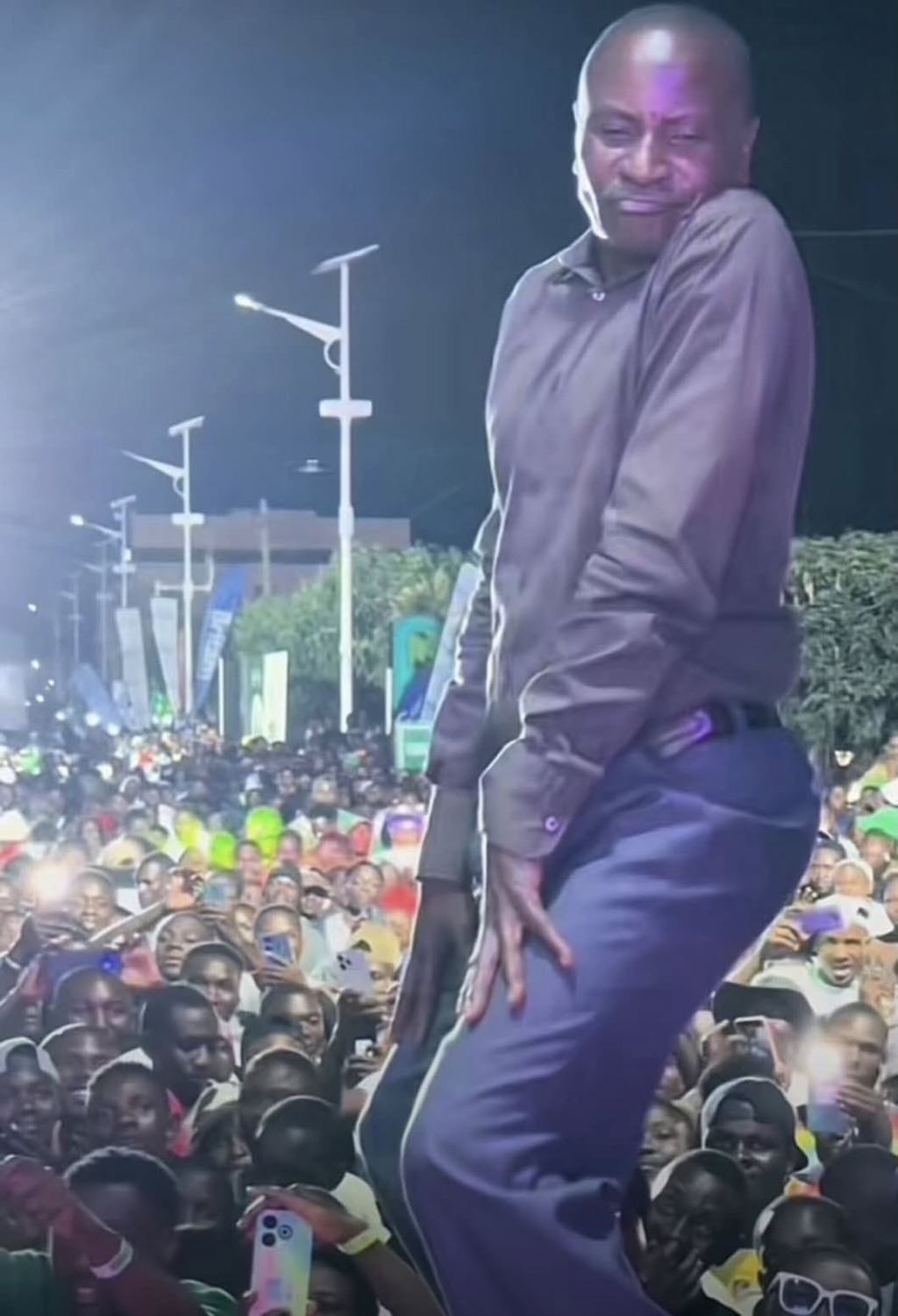 Man dancing on stage with a grin while a massive crowd films him
