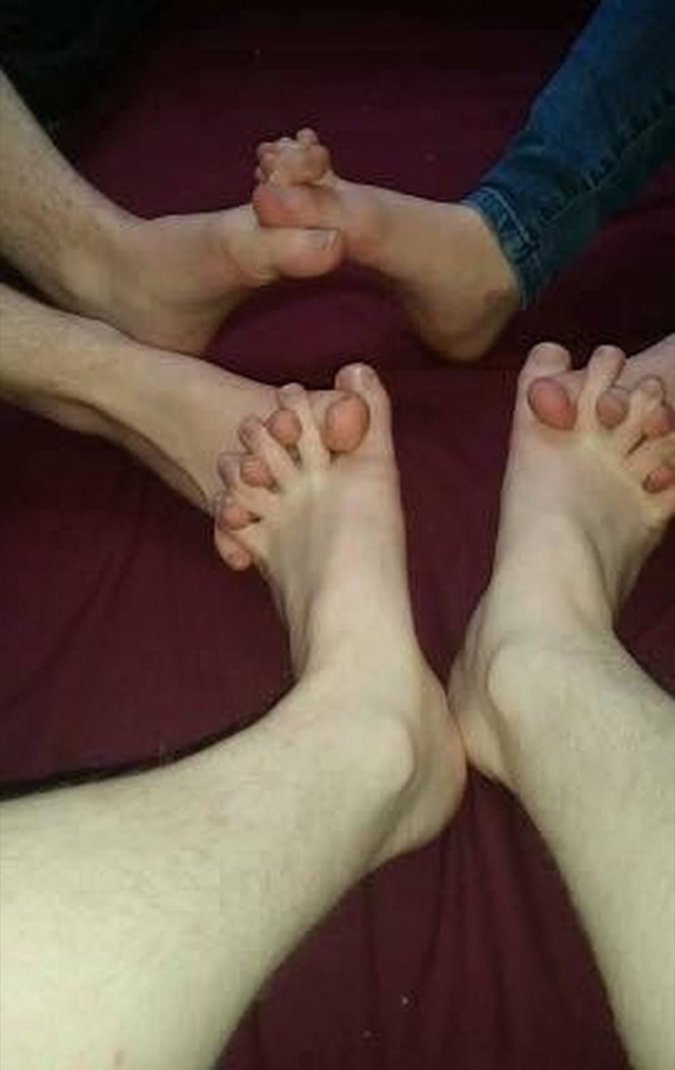 Multiple pairs of bare feet arranged in a circle on a burgundy surface — deeply confusing energy