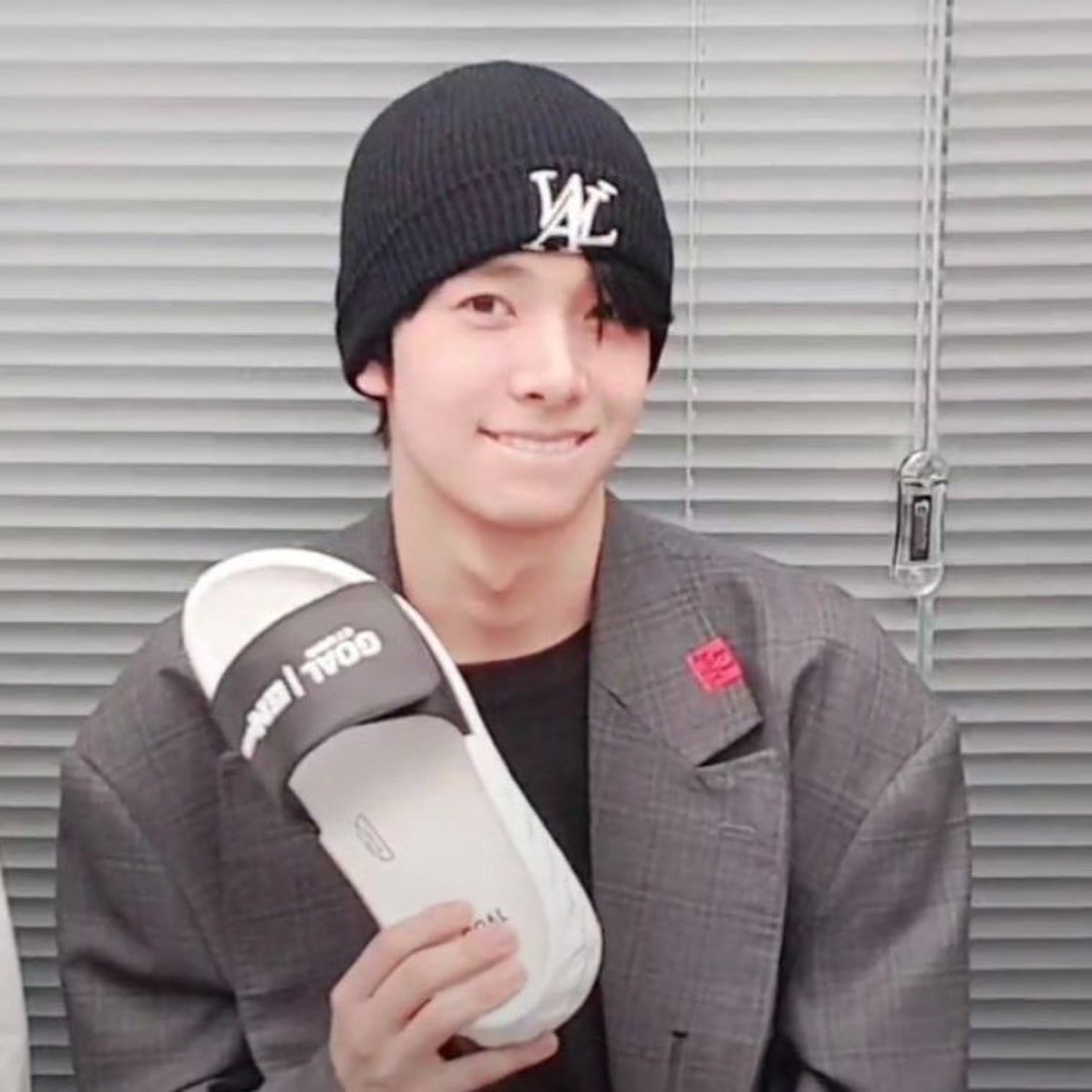 Young man in a black beanie holding up a pair of slides with a shy, pleased smile