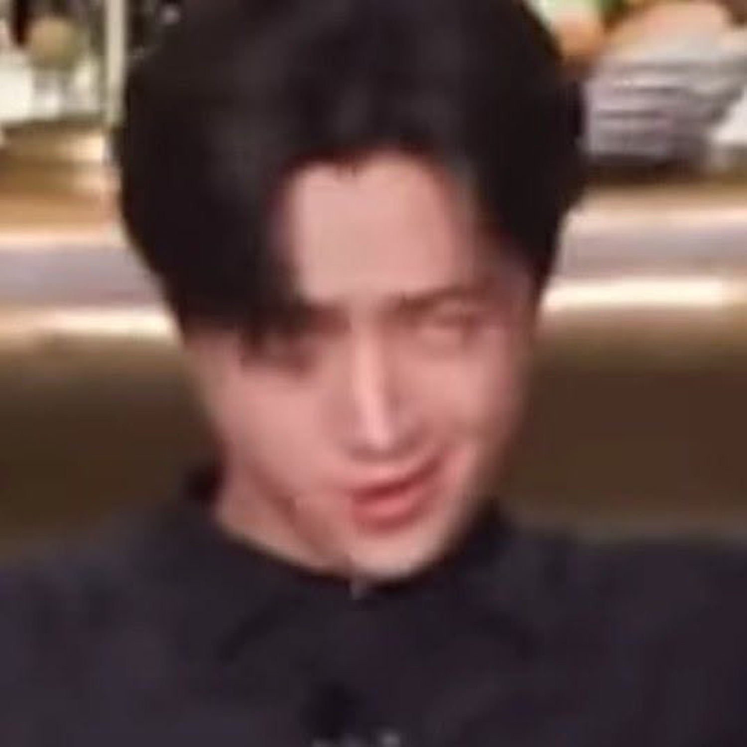 Dark-haired man in black shirt with a sly, self-satisfied smirk looking downward