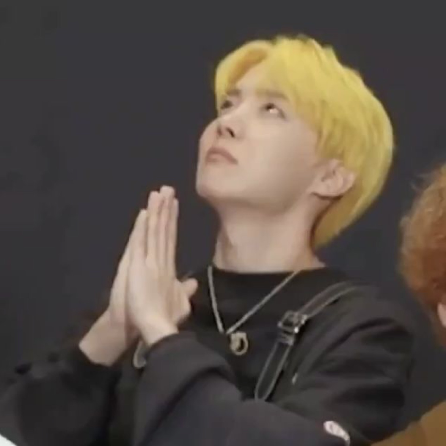 Blond-haired man pressing his hands together and looking upward as if praying