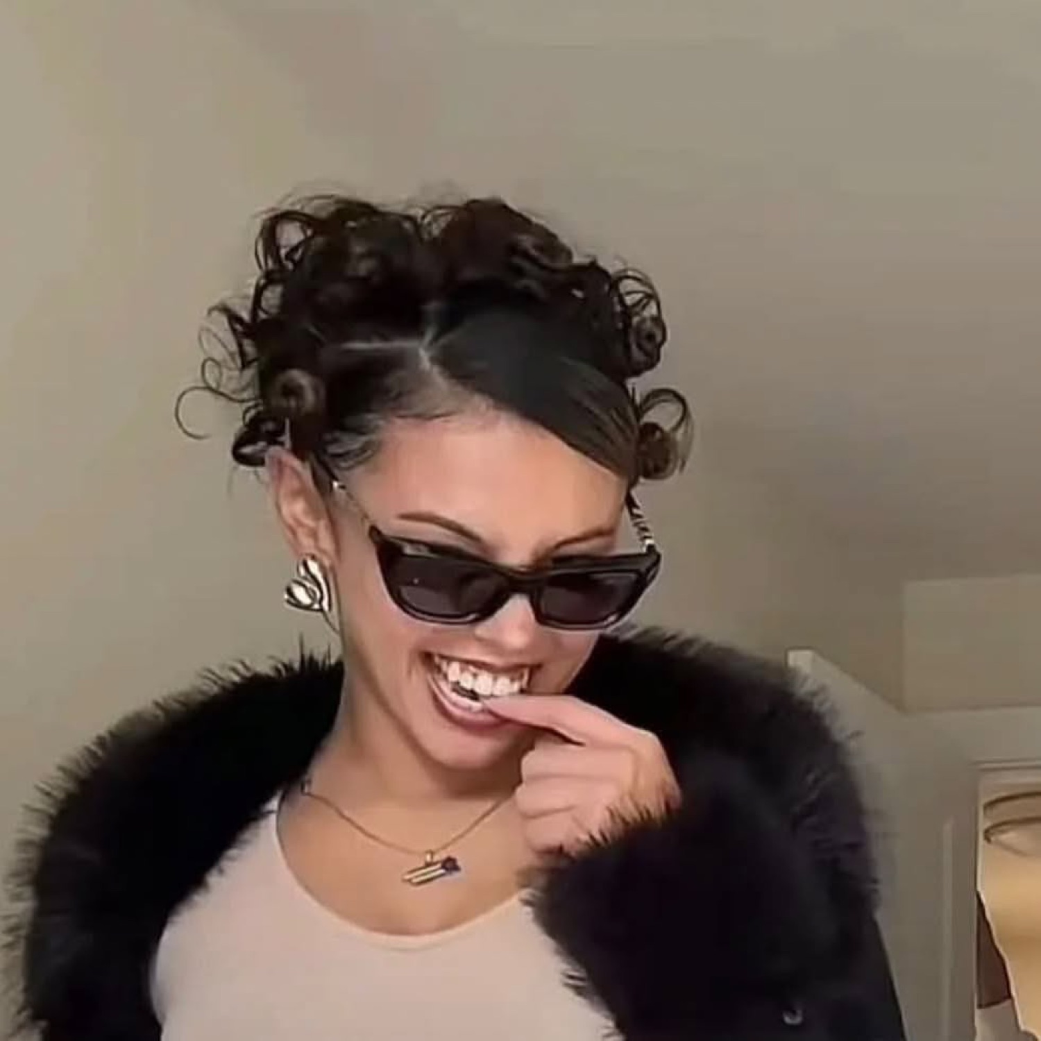 Woman in sunglasses and a fur coat grinning and biting her finger