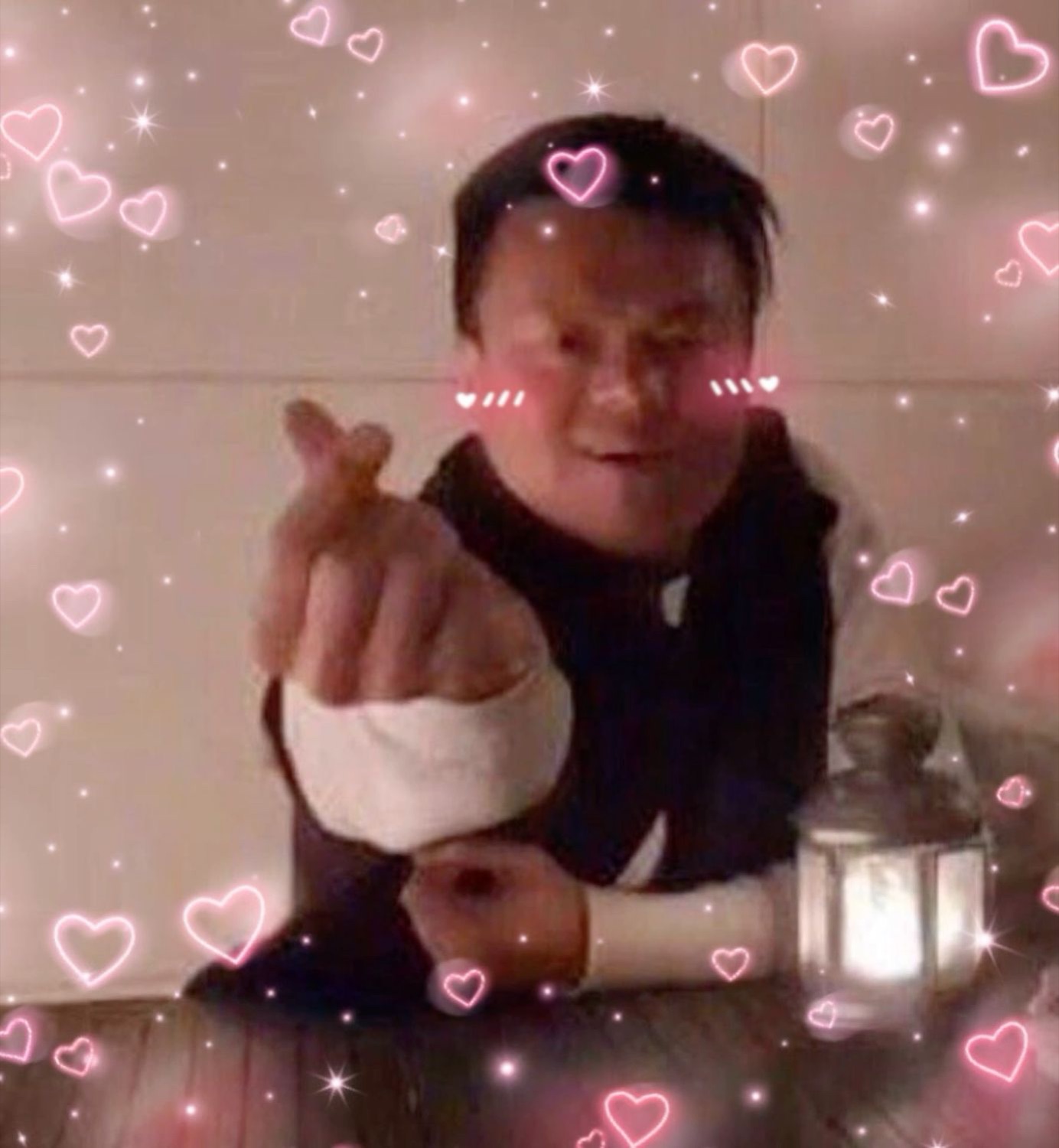 Man doing a finger heart gesture surrounded by pink hearts and sparkles filter