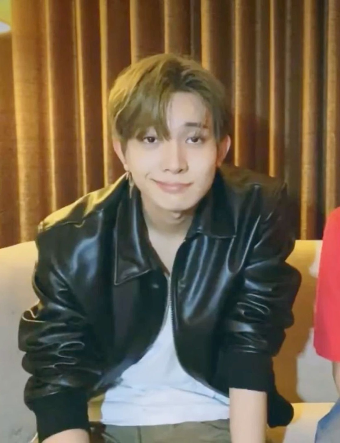 Young man in a black leather jacket giving a small, slightly smug closed-mouth smile