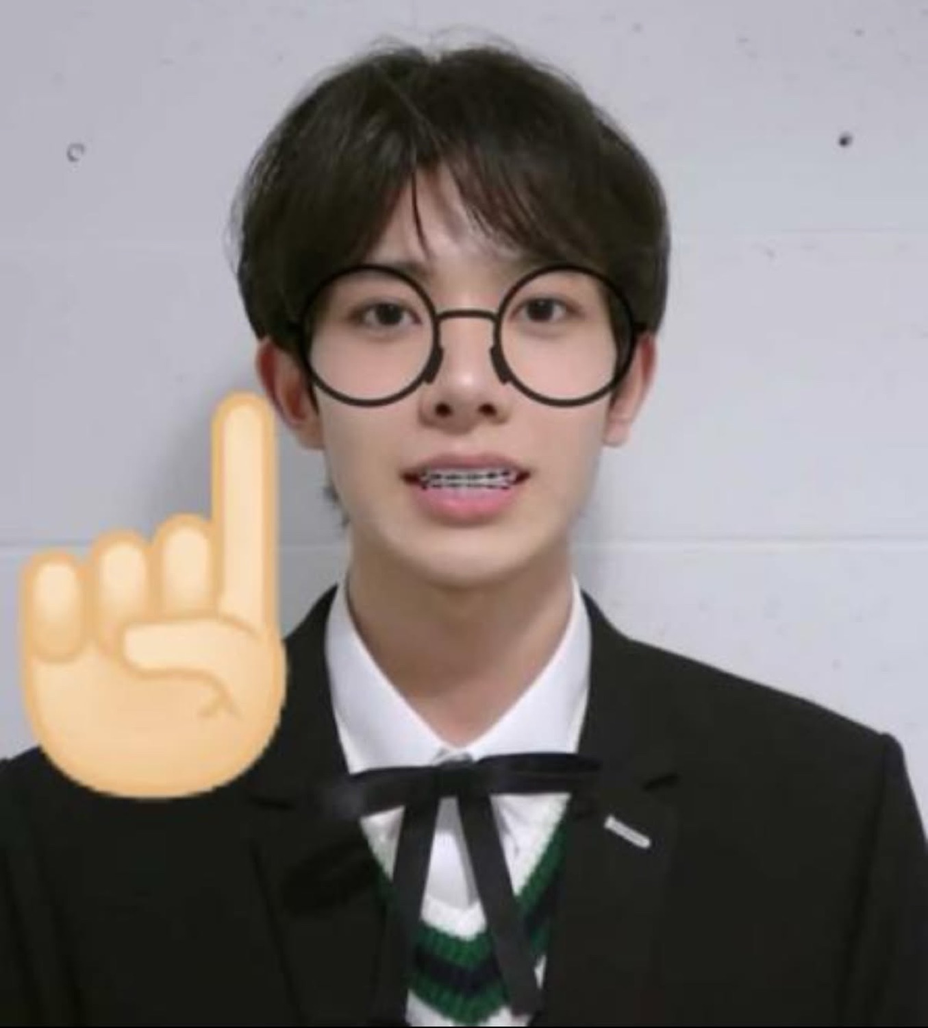 Young man in glasses and braces with an emoji pointing finger raised, making a point