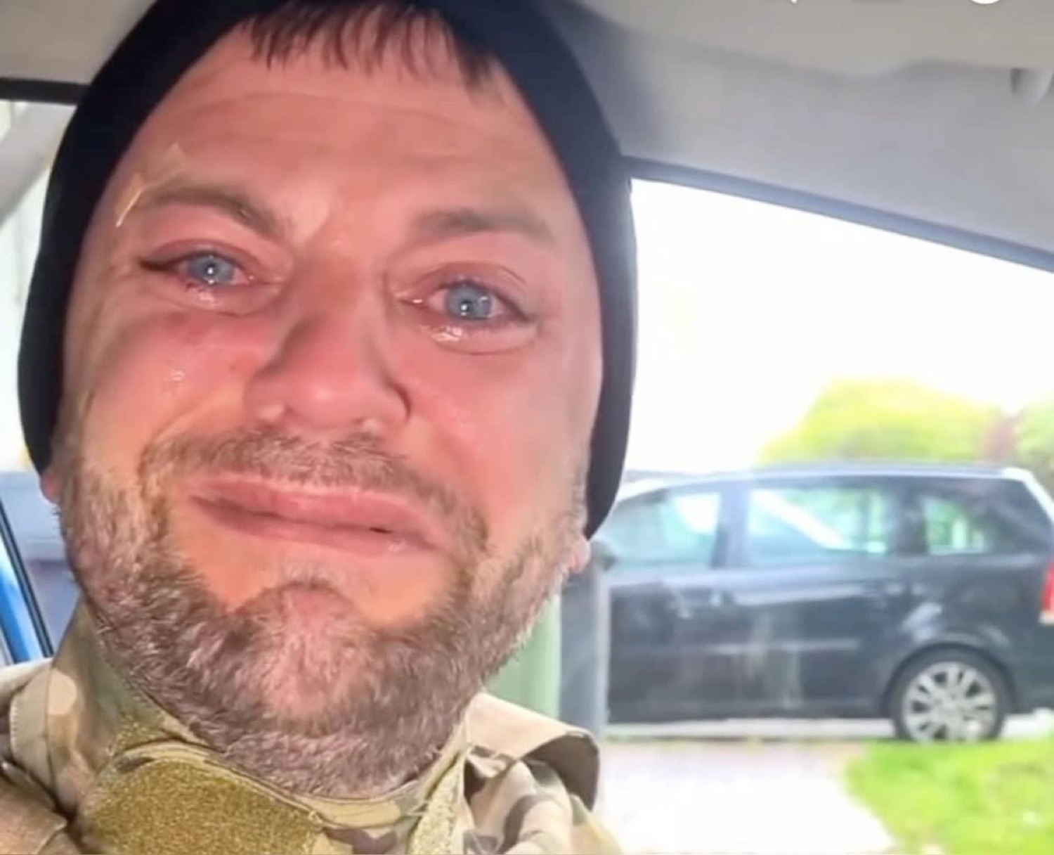 Man in military gear crying in his car with red-rimmed watery eyes