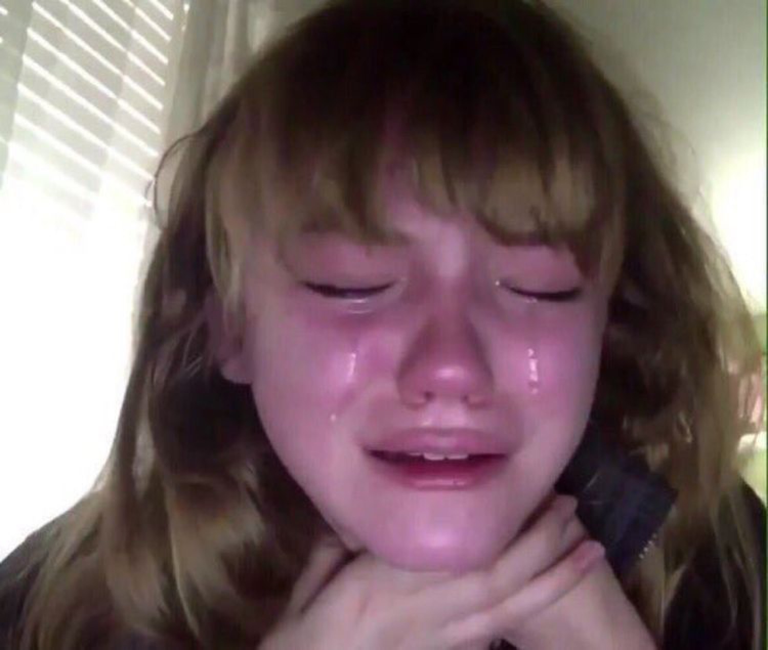 Girl with bangs crying softly with tears running down her face, hands under her chin