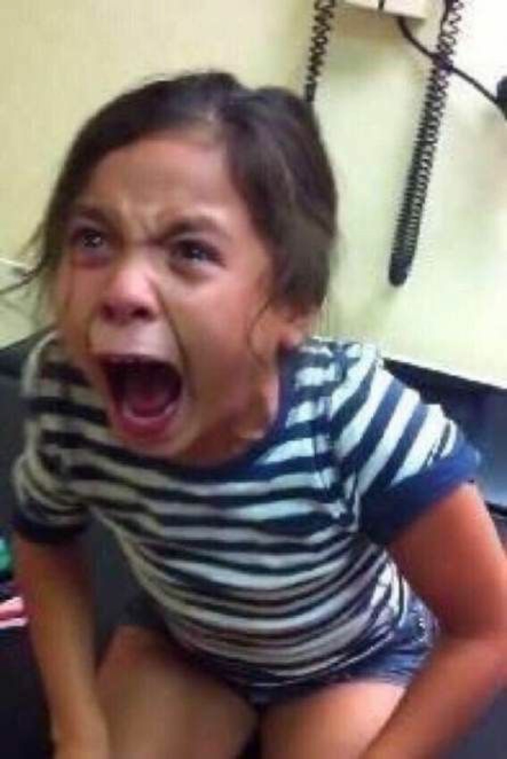 Little girl in a striped shirt screaming with mouth wide open in pure outrage