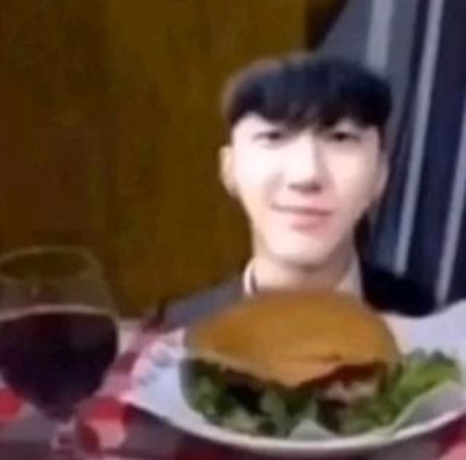 Young man smiling smugly behind a burger plate and glass of wine at a date setup