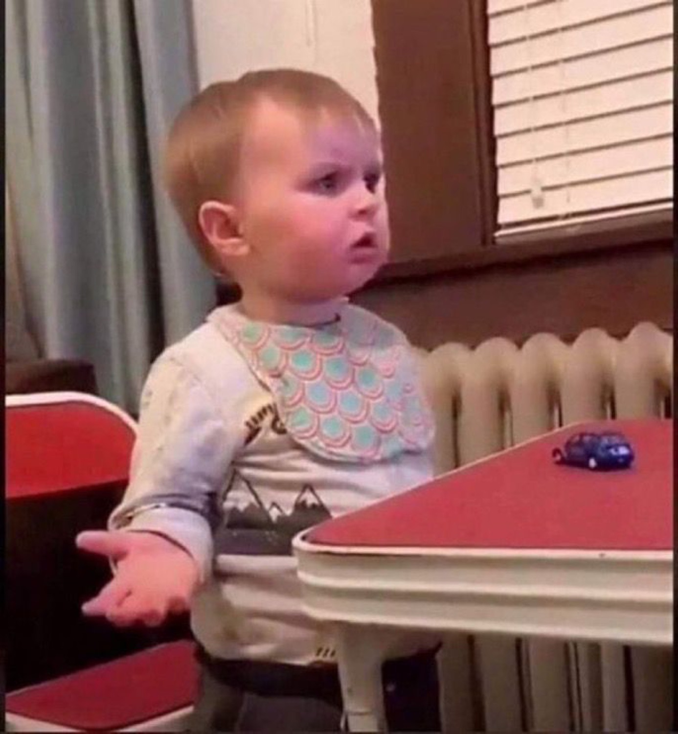 Toddler sitting at a tiny desk looking deeply unimpressed and mildly puzzled about something
