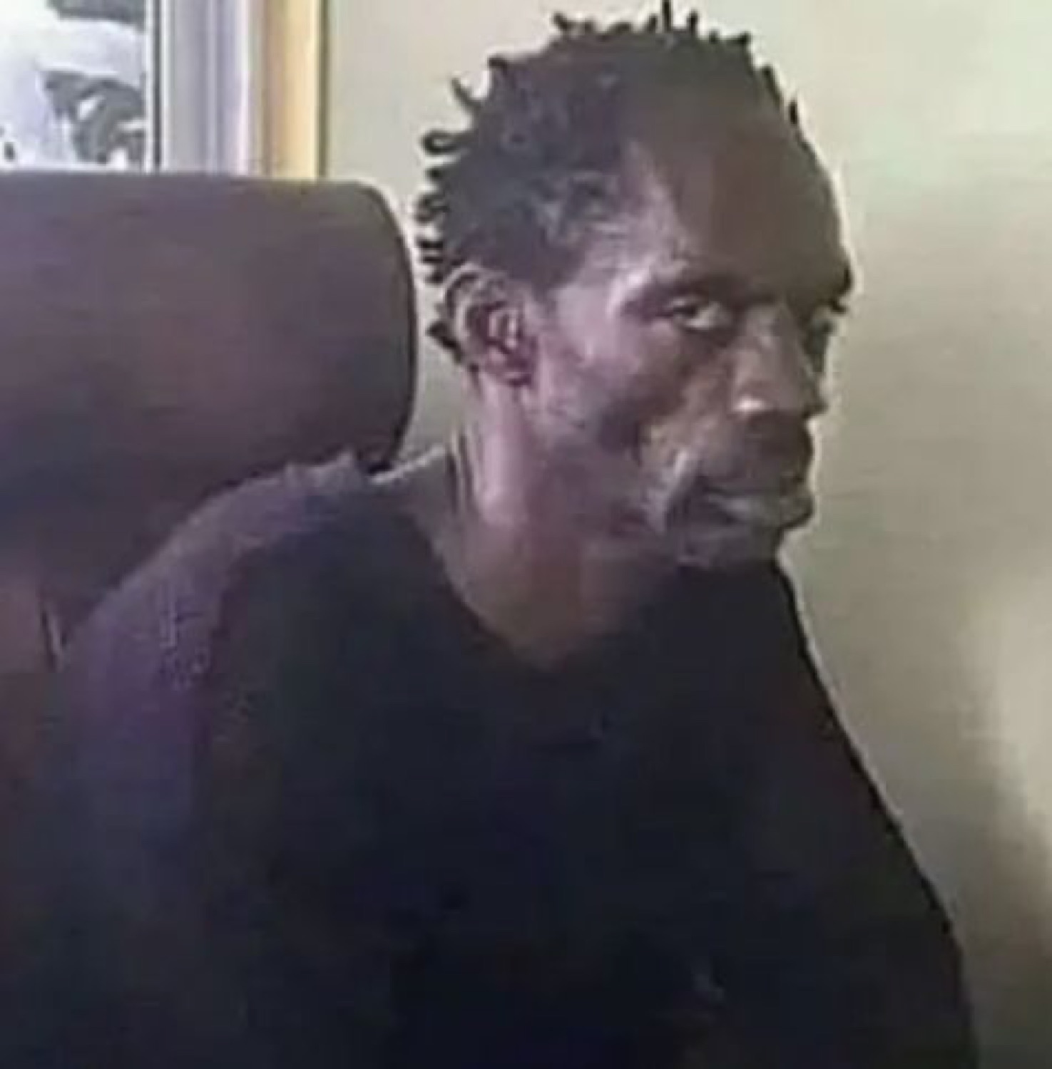 Thin man with twists sitting hunched, staring off with a hollow, haunted look