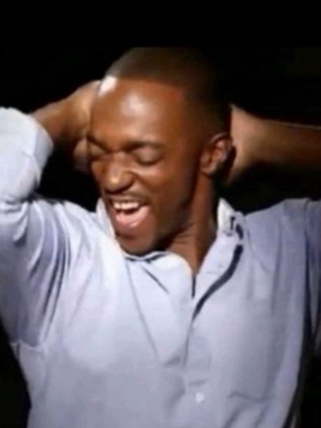 Man in a blue shirt cracking up with his hands behind his head and eyes squeezed shut