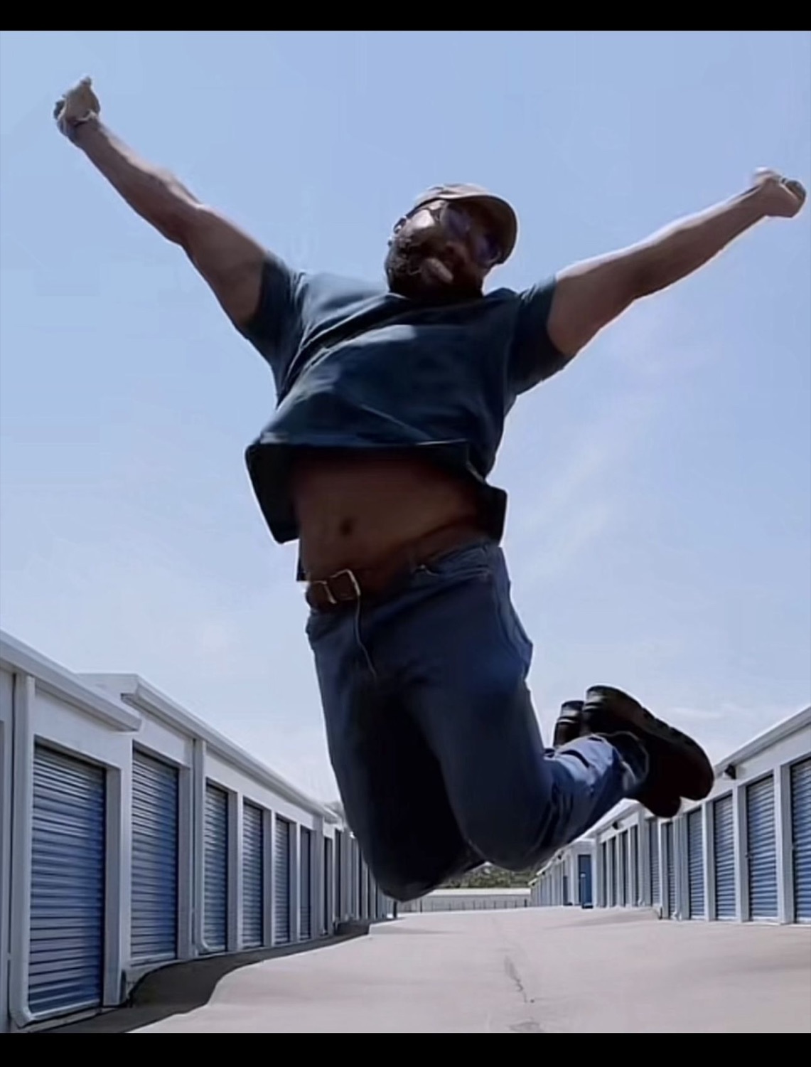 Man leaping into the air with arms spread wide between rows of storage units