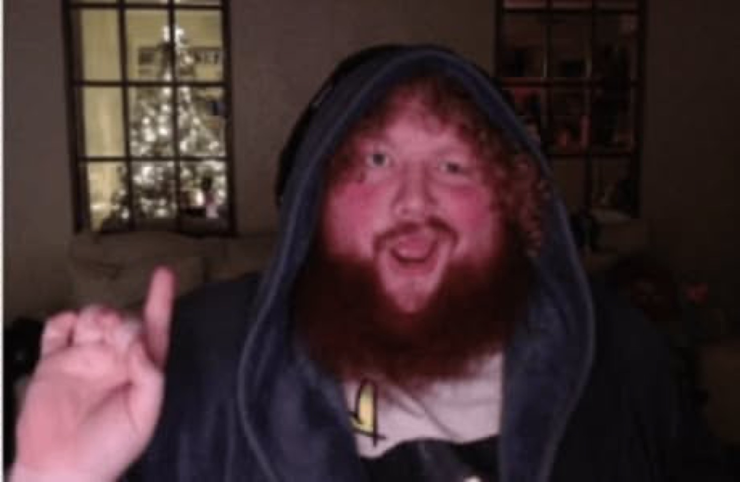 Bearded guy in a hoodie grinning wide with one finger raised mid-point