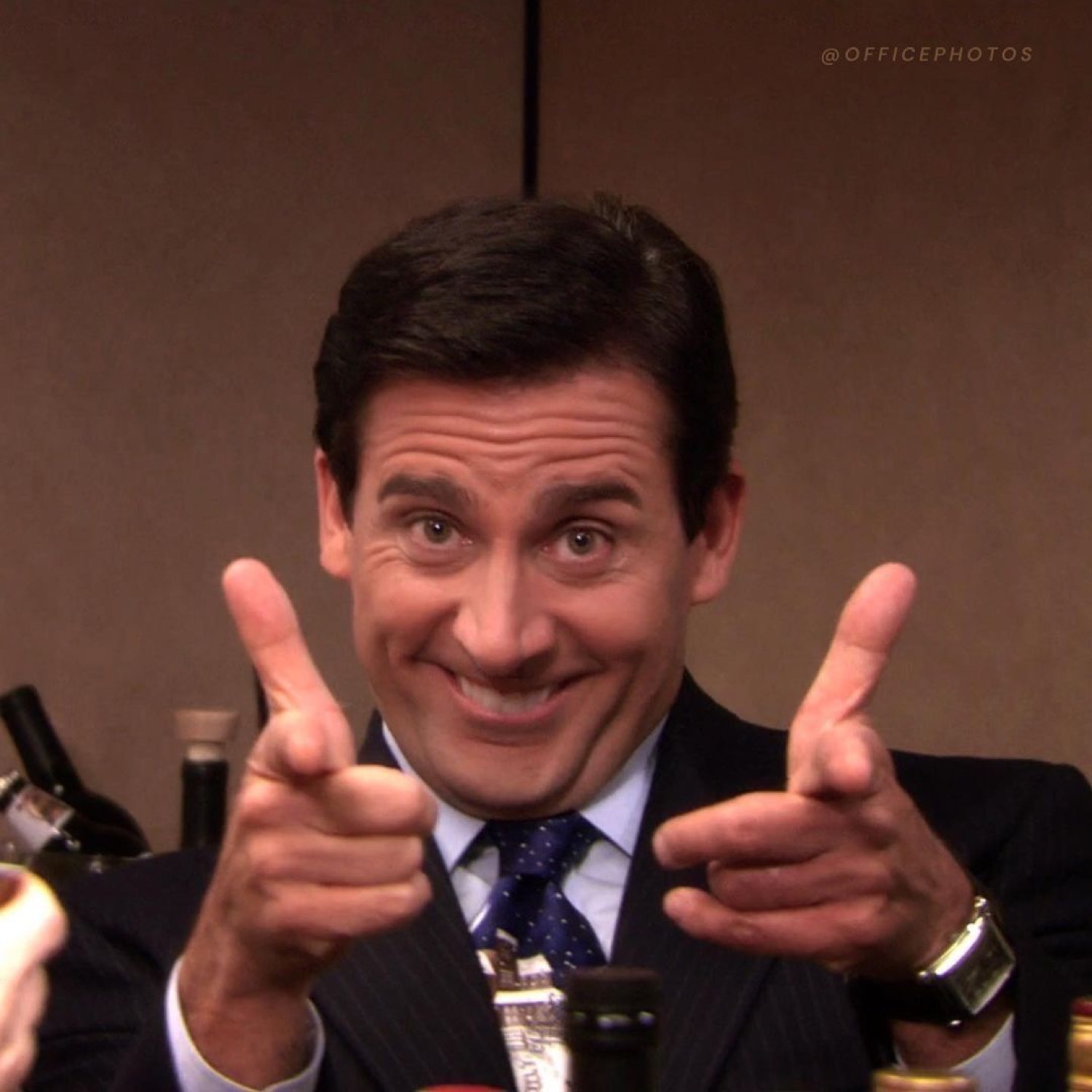 Michael Scott in a suit doing enthusiastic double finger guns with a big grin