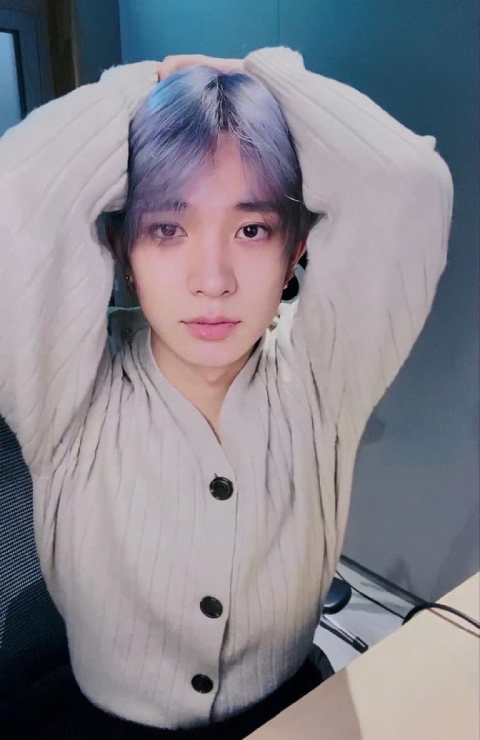 Lavender-haired guy with both arms up behind his head giving a flat, blank stare